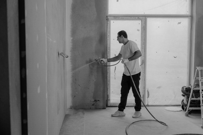 A worker paints an interior wall with a spray gun during a renovation project.